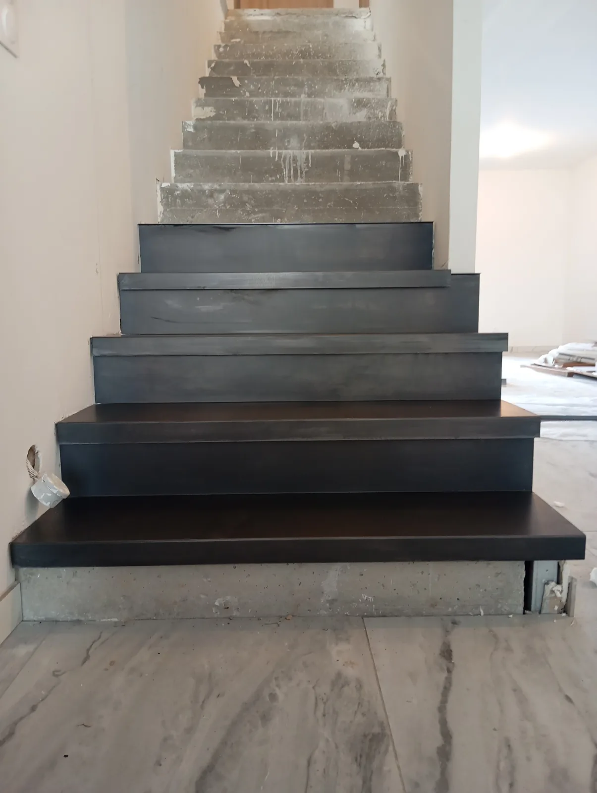 Habillage d'escalier béton en acier noir en cours, premières marches recouvertes